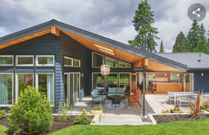 Modern home with a sleek design featuring large windows, a spacious patio with seating and a fire pit, surrounded by lush greenery and tall trees